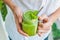 Mason jar mugs filled with green spinach, banana and coconut milk health smoothie with with a spoon of oatmeal In hands on wooden