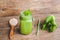 Mason jar mugs filled with green spinach, banana and coconut milk health smoothie with with a spoon of oatmeal on wooden rustic ta