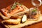 Mason jar with pieces of salmon with fresh cucumber, toasts and ruccola and served with parchment paper on wooden board in