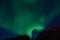 Massive aurora borealis dancing on night sky over mountain top