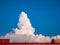 Massive cloud with spectacular shape rises high into the blue sky over the roof. The photo is framed by the roof of the house with