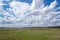 Massive cumulus white clouds in a blue sky over a green plain.