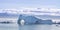 Massive iceberg with large arches set against a background of snow capped mountains in Qaqortoq