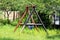 Massive old outdoor playground equipment swing with strong thick wooden frame and two plastic seats with faded colors