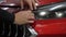 The master applies vinyl film to the headlight of a red car. Closeup view on worker detailer hand smoothing with a