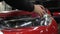 The master applies vinyl film to the headlight of a red car. Closeup view on worker detailer hand smoothing with a