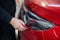 The master applies vinyl film to the headlight of a red car. Closeup view on worker detailer hand smoothing with a
