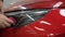 The master applies vinyl film to the headlight of a red car. Closeup view on worker detailer hand smoothing with a