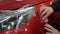 The master applies vinyl film to the headlight of a red car. Closeup view on worker detailer hand smoothing with a