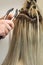 Master makes hair extensions to a woman. Close-up of the process. Vertical photo