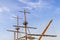 Masts, sail yards with the lowered sails and rigging of a sailing ship against a clear blue sky with white scenic clouds on a