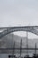 Masts of wooden rabelos boats, carrying wine barrels, docked on the Douro River in Porto, beneath the Don Luis I steel bridge in