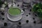 Matcha green tea in a porcelain mug on a grey textured background with flowers