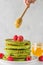 Matcha tea green pancakes. Pile of homemade pancakes with fresh raspberries and flowing honey. vertical orientation