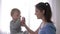 Maternal care, happy laughing toddler boy drinking pure mineral water from glass from smiling mother hands and rejoices