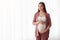 Maternity Concept. Portrait Of Smiling Pregnant Millennial Woman Standing Near Window