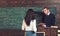 Math teacher pointing at green board. Professor giving explanations to brunette female student. Turn back girl in white