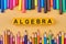Mathematics background with colorful pencils and inscription Algebra on color surface.