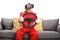Matrue man in a car racing suit wearing vr headset and holding a steering wheel seated on a sofa