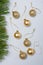 Matt and shiny golden bulbs on strings on light wooden background, plastic decorative Christmas baubles, pine tree branches border