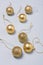 Matt and shiny golden bulbs on strings on light wooden background, plastic decorative Christmas baubles, vertical shot