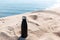 Matte black steel thermo bottle for water in sand of the beach on background of sea. Empty blank for mockup. Say no to plastic.