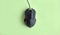 Matte modern black gaming mouse with buttons on a light green background.
