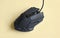 Matte modern black gaming mouse with buttons on a light yellow background