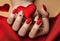 Matte red nails with small red heart on beige colour nail on the red fabric background. Saint Valentine\\\'s nail design