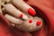 Matte red nails with small red heart on beige colour nail on the red fabric background. Saint Valentine\\\'s nail design