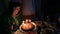 Mature adult woman of Caucasian ethnicity blows out candles on birthday cake, at festive table. Close-up.