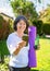 Mature adult woman practicing fitness outdoors holding bottle of water and yoga mat looking at online guide at smartphone.