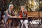 Mature Asian lady with positive grey haired friend spend time together in street cafe