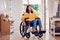 Mature Asian Woman In Wheelchair Pushing Herself Along Hallway At Home