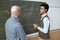 Mature bald professor and young mixed-race student discussing solution of equation by blackboard