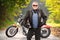 Mature biker in leather jacket standing in front of his chopper