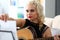 Mature blond woman turning notes pages while playing western acoustic guitar