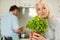 Mature blonde smiling at camera holding basil plant