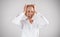 Mature business lady clenching her head and shouting in anger on light grey studio background