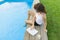 Mature business woman, freelancer, blogger with computer laptop and glass of water near the pool