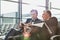 Mature businessman reading news paper while the other businessman is talking on smartphone in airport