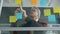 Mature businessman writing on sticky notes on office glass wall busy with business planning