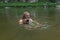 Mature caucasian man holding waterproof camera and swimming in river, trying to catch some interesting shots