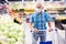 Mature caucasian man in mask with covid protection choosing head of cabbage in vegetable section of supermarket