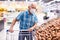 Mature caucasian man in mask with covid protection choosing potatoes in vegetable section of supermarke