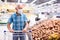 Mature caucasian man in mask with covid protection choosing potatoes in vegetable section of supermarke