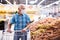 Mature caucasian man in mask with covid protection choosing potatoes in vegetable section of supermarke