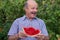 Mature caucasian man with mustache eating juicy water melon with pleasure and smiling.