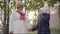 Mature Caucasian woman in beige cloche hat and white coat standing with her cheerful granddaughter in the yard of the