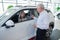 Mature Caucasian woman sits in a new car, an elderly man gives her the keys.